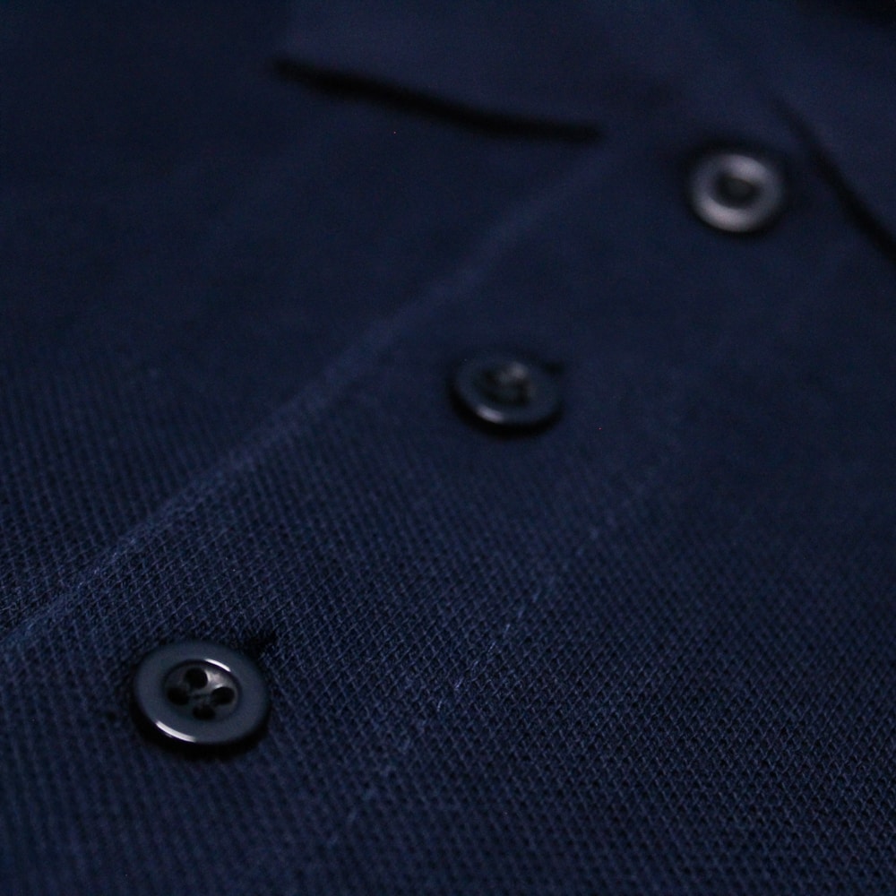 Navy blue shoulder stripe polo shirt with white striped detailing on sleeves, chest pocket, short sleeves, and three button placket on a plain background.